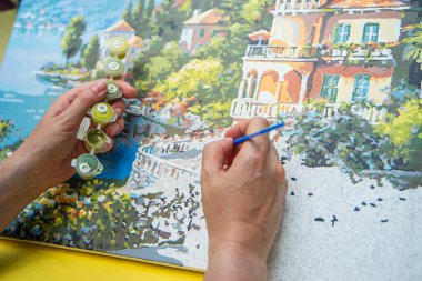 Painting for beginners, a woman draws a picture by numbers with acrylic paints on canvas artist draws a picture, painting a picture with a brush, a girl draws a picture, self-isolation, home hobby