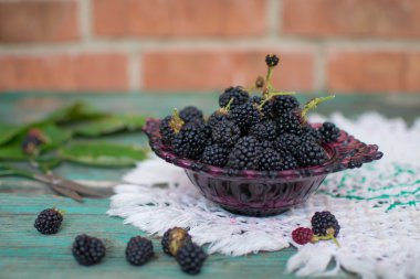 Mavi ahşap bir masa üzerinde şeffaf bir kase taze böğürtlen