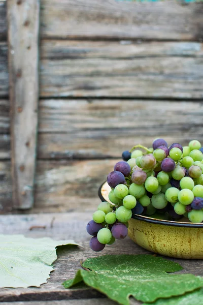 Raisins verts et noirs dans un bol sur fond bois, style rustique — Photo