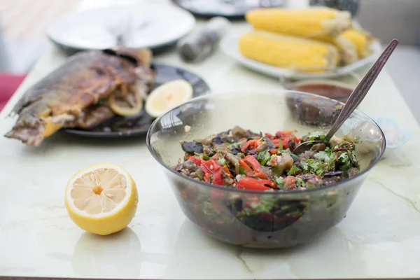 Cena di famiglia fatta in casa con una ciotola di insalata, pesce barbecue e mais dolce bollito sul retro — Foto Stock