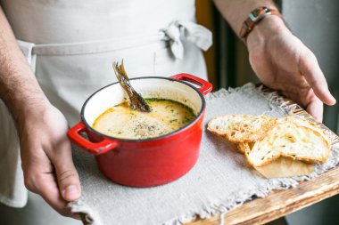 Küçük balık ekmek cips, erkek garson elleri ile bir gemide güzel bir küçük kırmızı tencerede Fin kremalı balık çorbası