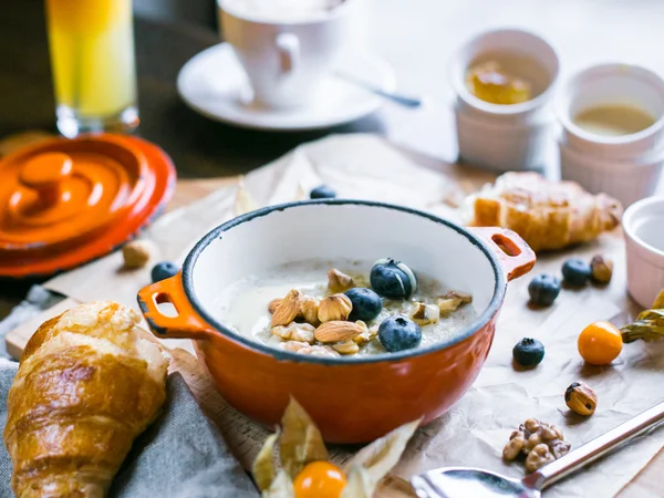 Petit déjeuner avec porridge et croissant décoré de bleuets et de noix, verre de jus d'orange et cappuccino — Photo