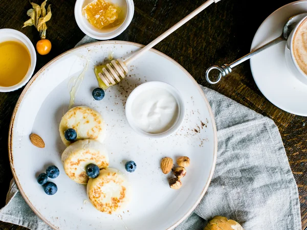 Сніданок з міні сирниками, ягодами, горіхами та медом на білій тарілці зверху — стокове фото