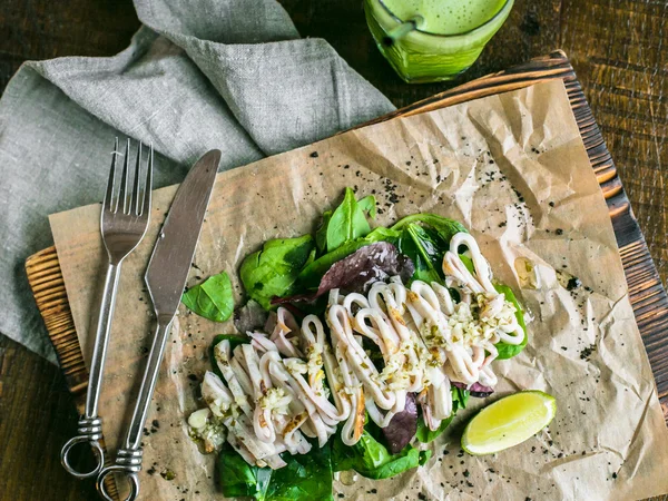 Kızarmış kalamar ve arka plan üzerinde bir kurulu, yeşil suyu limon ve Yeşiller ve limon kama ile