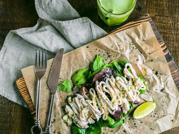 Kızarmış kalamar ve arka plan üzerinde bir kurulu, yeşil suyu limon ve Yeşiller ve limon kama ile