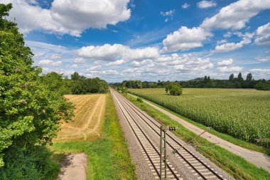 Demiryolu rayları, arka planda beyaz bulutlar ve mavi gökyüzü ile paralel uzanır.