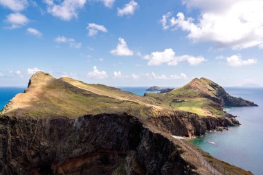 Turkuaz okyanusa bakan kayalıkları olan yeşil kıyı burnu, dağınık bulutlar altında çimenli sırt ve kayalık kayalık kayalıklar, sakin keşifleri ve uzak yaz ıssızlığını çağrıştıran panoramik bakış açısı