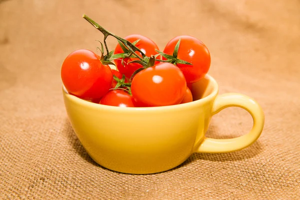 Tomates rojos cherry en una taza amarilla sobre tela vieja — Foto de Stock