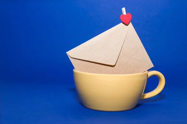 Envelope with heart  in the yellow cup on a blue background. — Stock Photo, Image