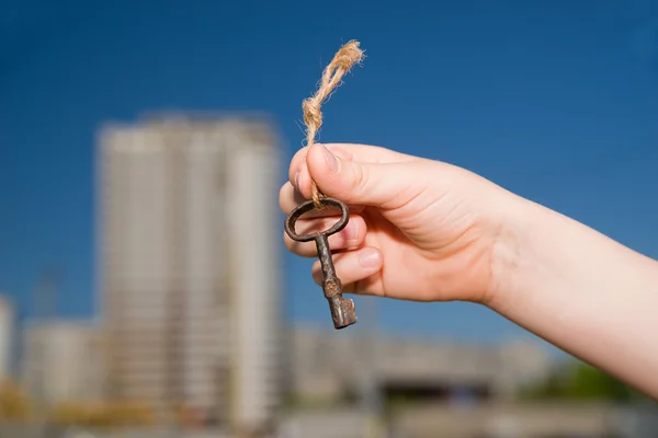 Child hand holding an old key to the house against the sky — Stock Photo, Image