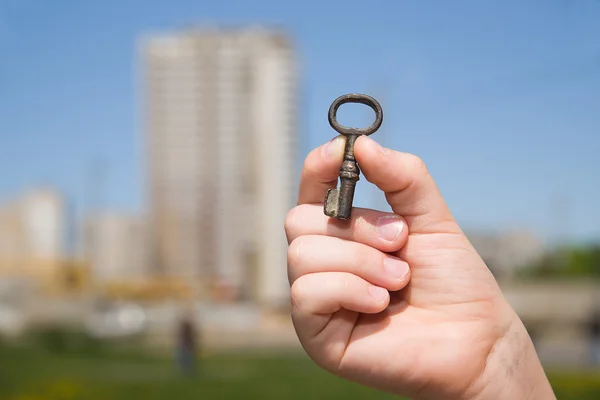 Main d'enfant tenant une vieille clé de la maison contre le ciel — Photo