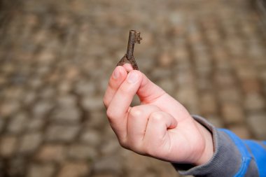 Child's hand holding one old key clipart