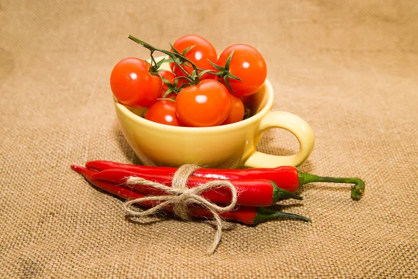Red cherry tomatoes in a yellow cup and Chile peppers  on old cl — Stock Photo, Image