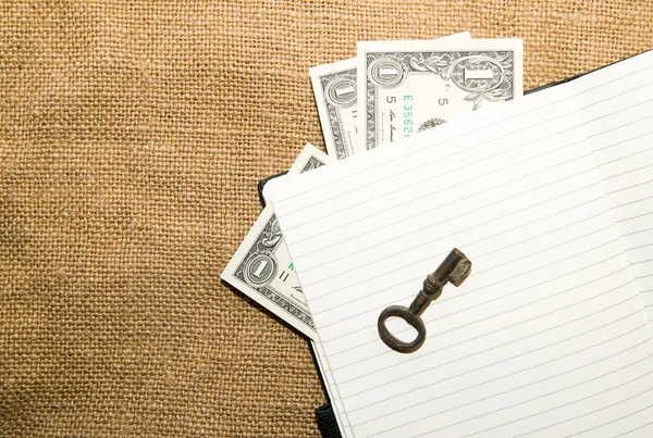 Opened notebook, key and money on the old tissue — Stock Photo, Image