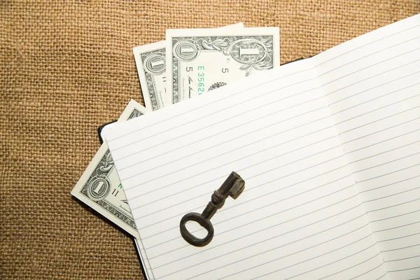 Opened notebook, key and money on the old tissue — Stock Photo, Image