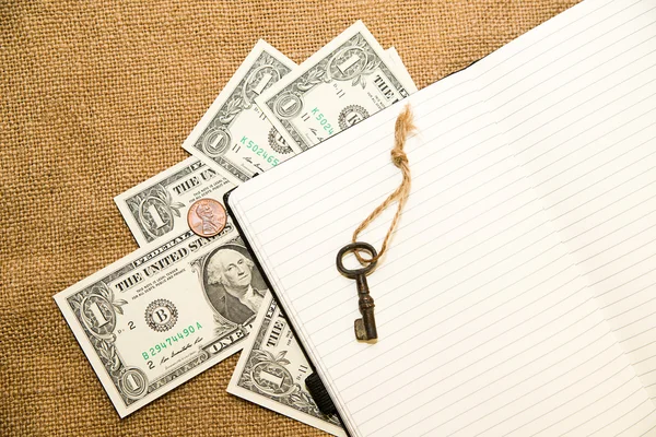 Opened notebook, key and money on the old tissue — Stock Photo, Image