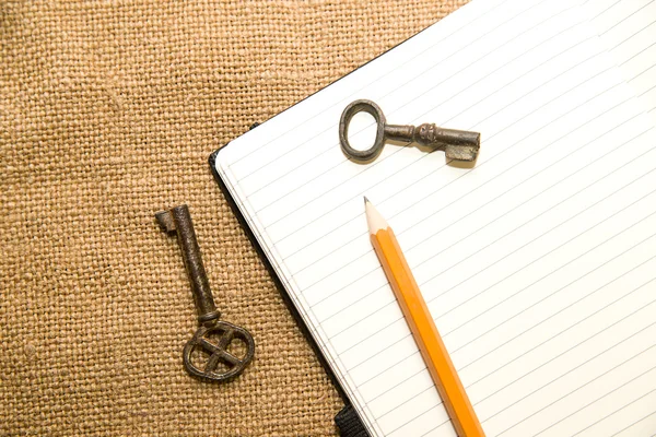 Opened notebook, keys and pencil on the old tissue — Stock Photo, Image