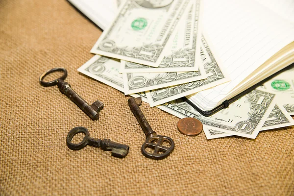 Opened notebook, keys and money on the old tissue — Stock Photo, Image