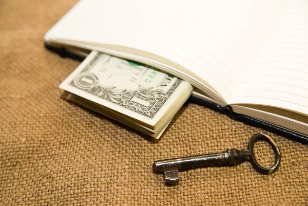 Quaderno aperto, chiave e denaro sul vecchio tessuto — Foto Stock
