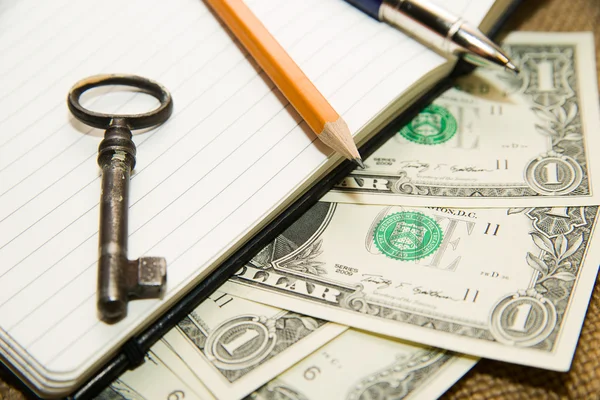 Opened notebook, pencil, pen,  key and money on the old tissue — Stock Photo, Image