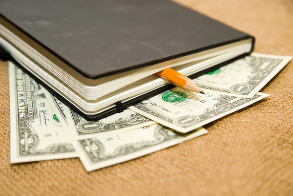 Ноутбук, карандаш и деньги на старой ткани — стоковое фото