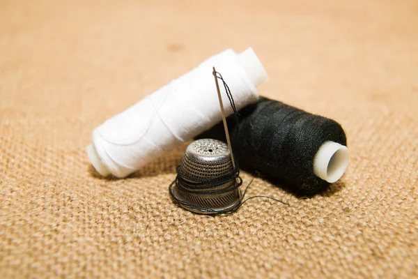 Needle, thimble and thread spool on the old cloth — Stock Photo, Image