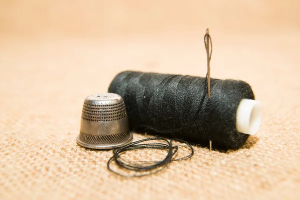 Needle, thimble and thread spool on the old cloth — Stock Photo, Image