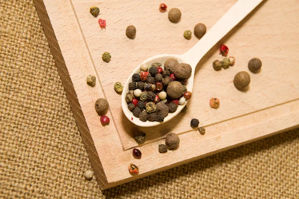 Cucchiaio riempito con una miscela di grani di pepe sono su un legno — Foto Stock