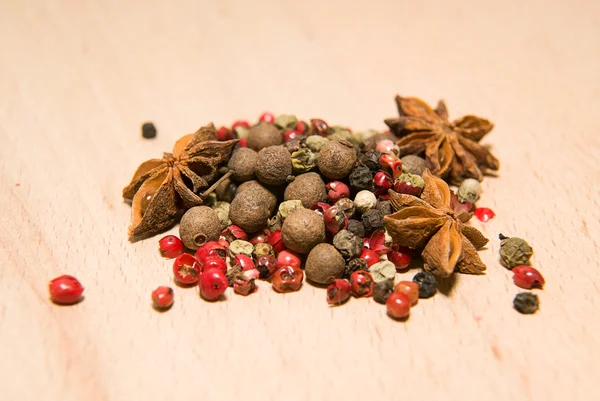 Uma mistura de grãos de pimenta e anis estrelado em uma superfície de madeira — Fotografia de Stock