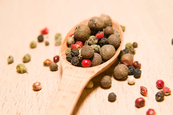 Cuillère remplie d'un mélange de grains de poivre sont sur un bois — Photo