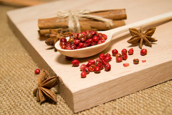 Cucchiaio pieno di grani di pepe e anice stellato su un su di legno — Foto Stock