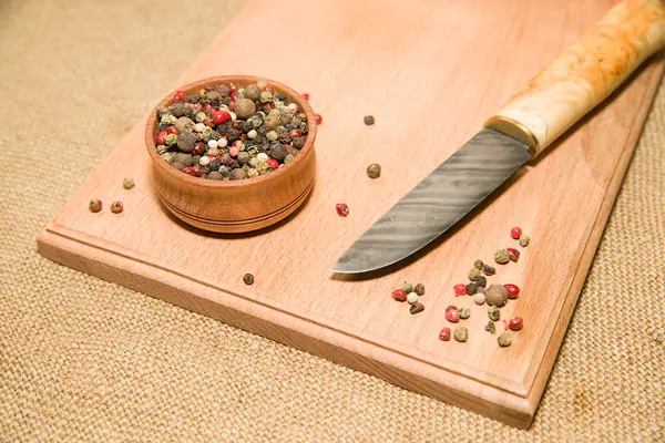 Il coltello, una miscela di grani di pepe su una superficie di legno — Foto Stock