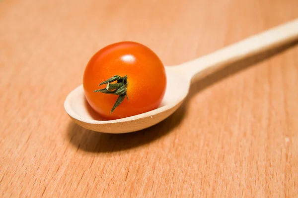 Tomate rojo en una cuchara de madera sobre una superficie de madera — Foto de Stock