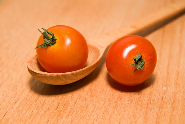 Tomates vermelhos em uma colher de madeira em uma superfície de madeira — Fotografia de Stock