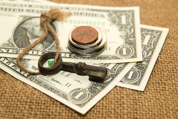 US dollars banknotes, coins and key on an old cloth — Stock Photo, Image