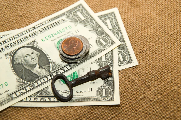 US dollars banknotes, coins and key on an old cloth — Stock Photo, Image