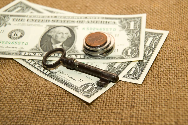 US dollars banknotes, coins and key on an old cloth — Stock Photo, Image