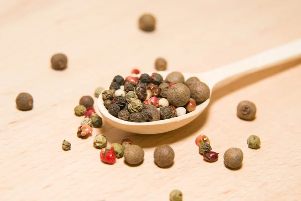 Cucchiaio pieno di grani di pepe su una superficie di legno — Foto Stock
