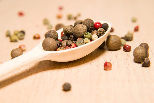 Cucchiaio pieno di grani di pepe su una superficie di legno — Foto Stock