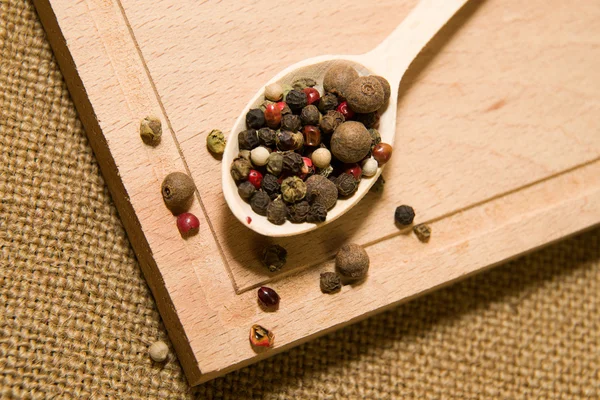 Colher cheia de grãos de pimenta em uma superfície de madeira — Fotografia de Stock