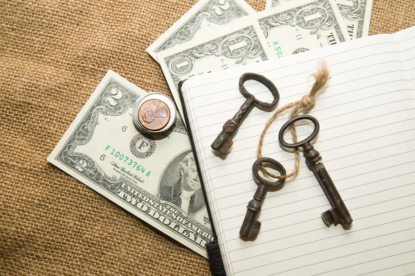 Opened notebook, keys and money on the old tissue — Stock Photo, Image