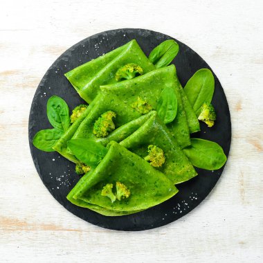 Vejetaryen yemeği. Siyah taş tabakta sebzeli yeşil ıspanaklı krep. Üst Manzara. Metnin için boş yer.