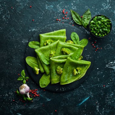 Vejetaryen yemeği. Siyah taş tabakta sebzeli yeşil ıspanaklı krep. Üst Manzara. Metnin için boş yer.