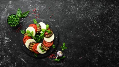 Fesleğenli Caprese salatası. Siyah taş tabakta domates, mozarella peyniri ve patlıcan. Üst Manzara. Metnin için boş yer.