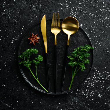 Siyah taşlı arka planda siyah tabak ve çatal bıçak takımı. Üst Manzara. Metin için boş alan.