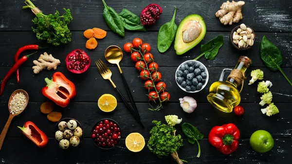 Food background: A set of healthy and clean food - vegetables, fruits, fish, meat, nuts and greens. On a black stone background. Top view. Free copy space.