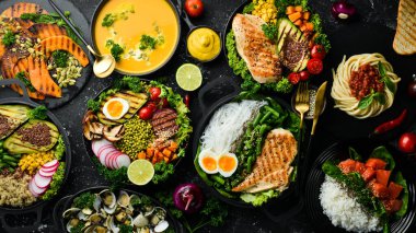 Yemek geçmişi: makarna, tavuk, balkabağı, salata, et, mantar, sebze. Siyah taştan bir arka planda. Üst Manzara. Metin için boş alan.