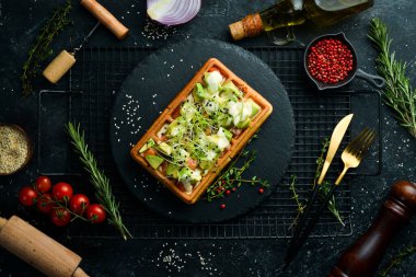 Kahvaltıda. Belçika waffleları: avokado, tuzlu balık ve mikroyeşil. Siyah taştan bir tabakta.