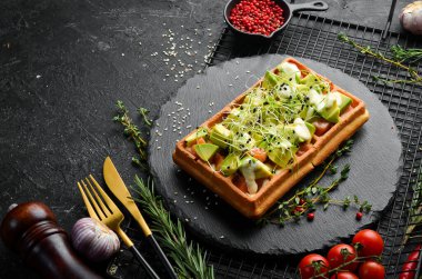 Kahvaltıda. Belçika waffleları: avokado, tuzlu balık ve mikroyeşil. Siyah taştan bir tabakta.
