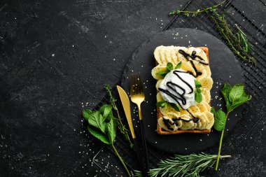 Belçika waffle 'ı: muzlu, dondurmalı ve çikolatalı. Tatlı. Siyah taştan bir tabakta.